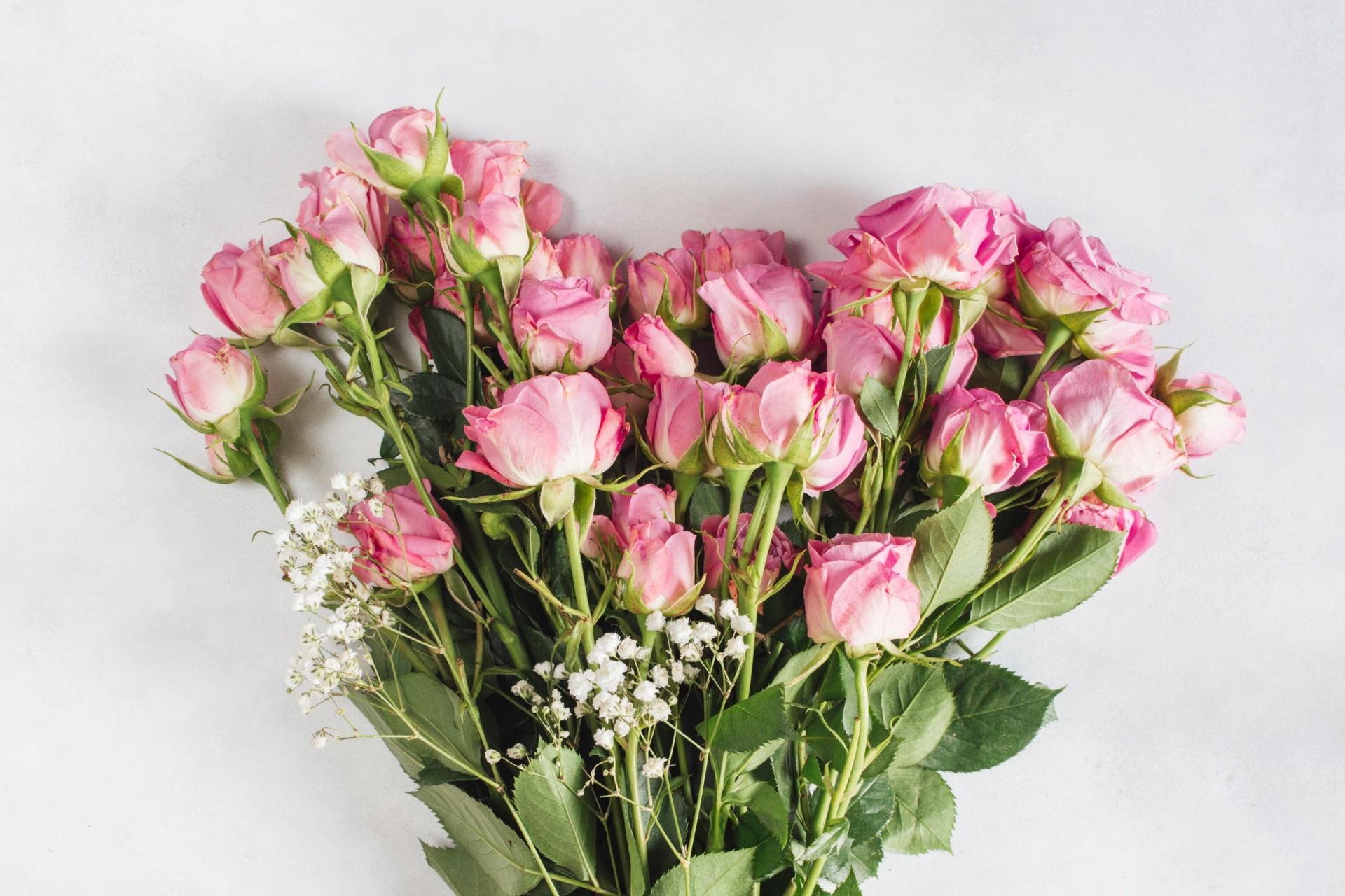 Herzförmig angeordneter Blumenstrauß aus rosa Rosen und zwei Zweigen Schleierkraut